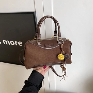 Sac à main Boston en daim marron avec nœud et breloque en fourrure tenu à la main
