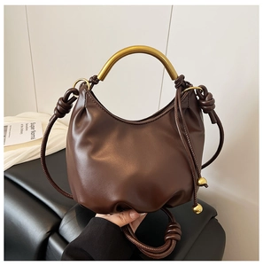 Detail view of brown cloud bag with gold metal handle and braided strap accents