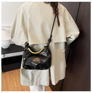 Detail of black cloud shoulder bag featuring a gold curved handle and knotted strap