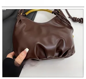 Close-up of brown ruched cloud bag featuring elegant gold arched handle and soft PU leather