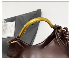 Detail of dark brown cloud bag featuring a golden arched metal handle and knotted leather