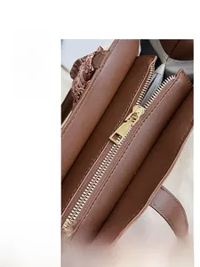 Close-up of smooth gold metal zipper and silk scarf detail on a brown leather tote bag