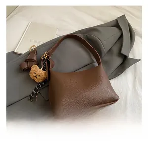 Detail of dark brown lychee leather handbag with a plush bear charm and woven ornament