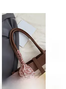 Close-up of brown leather tote bag with red and white paisley silk scarf on handle