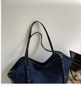 Detail of navy denim tote bag featuring sturdy black leather handles and silver hardware