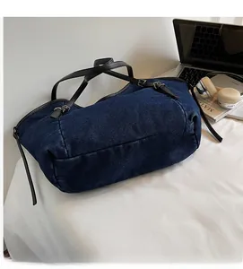 Detail of blue denim tote bag with black leather straps and silver buckles for commute