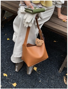Detail of brown lychee grain leather crossbody bag with a plush bear charm accessory