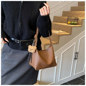Detailed texture of brown litchi grain leather shoulder bag with cute bear charm detail