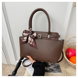 Detailed view of brown lychee grain leather handbag with silk scarf on a straw chair
