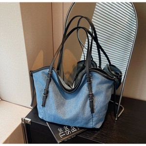 Detailed macro view of the blue denim tote bag with black leather straps and metal buckle