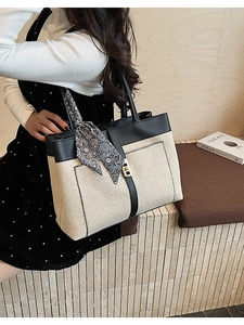 Detail of canvas tote bag with black faux leather trim, gold lock, and paisley scarf