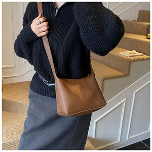 Detail of a brown lychee pattern leather crossbody bucket bag worn by a model