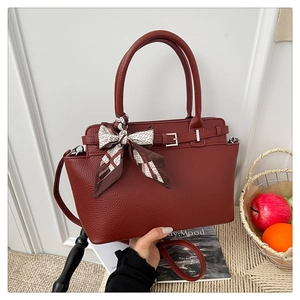 Detail of burgundy lychee leather handbag with silk scarf on woven background