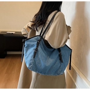 Detail of blue denim tote bag with black leather straps and metal buckle on shoulder