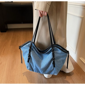 Detail of the blue denim tote bag featuring side metal buckles and leather handles