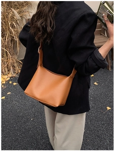 Outdoor street style view of a caramel brown lychee leather bucket bag with wide strap