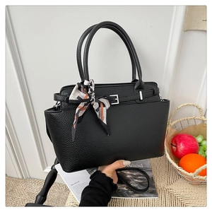 Macro detail of black litchi texture handbag with silver buckle and printed silk scarf