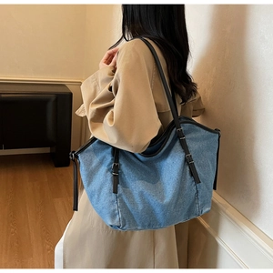 Detail of light blue denim tote bag with black leather straps on model shoulder