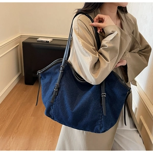 Detail of blue denim tote bag with black leather shoulder strap and silver metal buckle