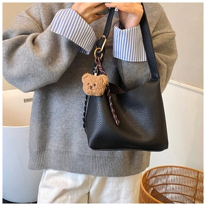 Detail of black pebbled leather crossbody bag featuring a cute brown plush bear charm