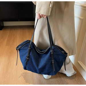 Close-up of blue denim tote bag with black leather straps and silver buckle detail