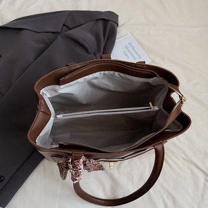 Detailed interior of a brown tote bag featuring a zipper compartment and silk scarf accent