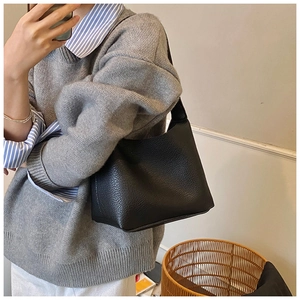 Side view of a minimalist black lychee grain leather crossbody bag on a model shoulder