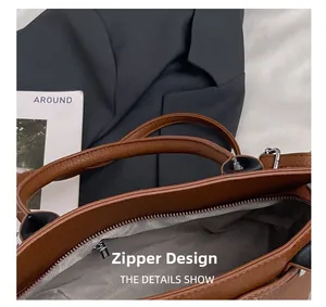 Detailed close-up of brown litchi grain leather handbag featuring smooth zipper closure