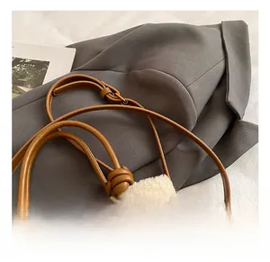 Detail of adjustable leather strap on check pattern handbag with wool trim and orange pompom