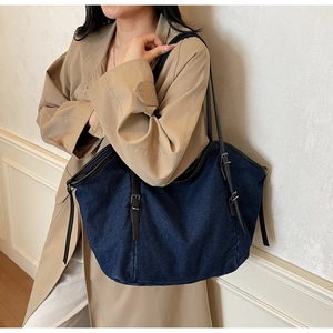 Detail of blue denim tote bag featuring black leather straps and metal adjustable buckles