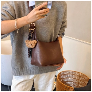 Detail of dark brown litchi pattern shoulder bag with golden rings and bear charm