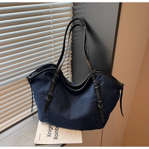 Detail of dark blue denim tote bag with leather straps and silver buckle adjustments