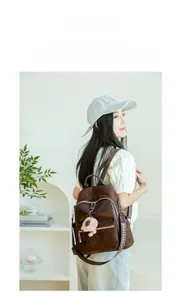 Detail eines dunkelbraunen Lederrucksacks mit Steppmuster und Plüsch-Pompon-Anhänger
