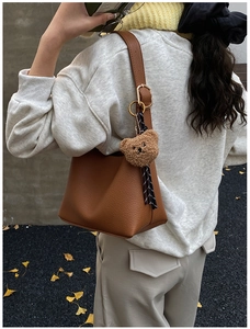 Close-up of brown pebbled leather shoulder bag with plush bear charm and autumn vibe