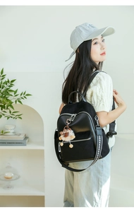 Detail eines schwarzen Rucksacks mit Steppmuster, Webriemen und Plüsch-Anhänger