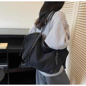 Close-up of a large black canvas tote bag with adjustable leather straps on model's shoulder