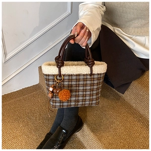 Detail of wool plaid handbag featuring plush trim and a brown pompom heart charm