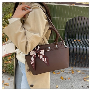 Detail of a brown lychee pattern handbag with a decorative silk scarf and adjustable strap