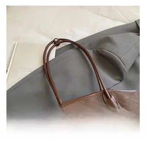 Détail du sac fourre-tout tressé marron foncé avec anse nouée sur un fond en tissu gris