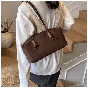Détail du sac cabas marron foncé en cuir tressé avec poignées nouées, porté par un mannequin