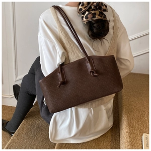 Détail d'un sac cabas tressé marron foncé avec nceud en cuir dans un cadre de vie quotidien