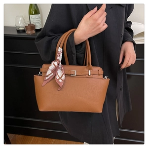 Close-up of brown lychee grain leather handbag with silk scarf detail on handle