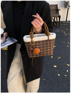 Detail of plaid wool tote bag with faux fur trim, leather handle, and plush ball charm