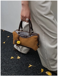 Détail du sac Boston en daim fauve avec garniture en cuir, nœud et breloque à pompon