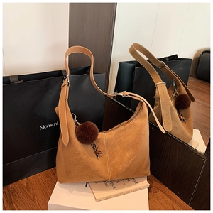 Detail of camel suede tote bag featuring a plush charm and adjustable metal buckle