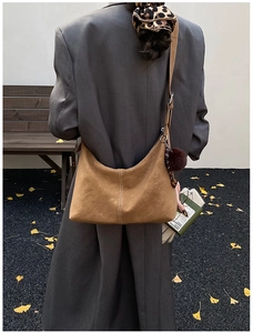 Detailed view of brown suede hobo bag with contrast stitching and fur pompom accessory