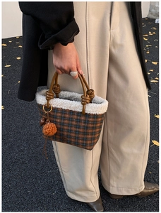 Detail of plaid tote bag with brown leather knotted handle and orange pompom accessory