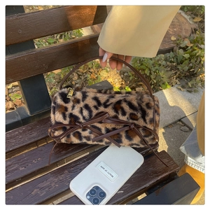Detail of leopard print plush barrel bag with leather bow and gold zipper on wooden bench