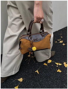 Sac Boston en daim marron avec garniture en cuir et breloque pompon tenu par un modèle