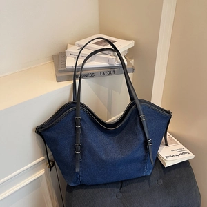 Large vintage denim tote bag with black leather handles and silver buckles on a bench